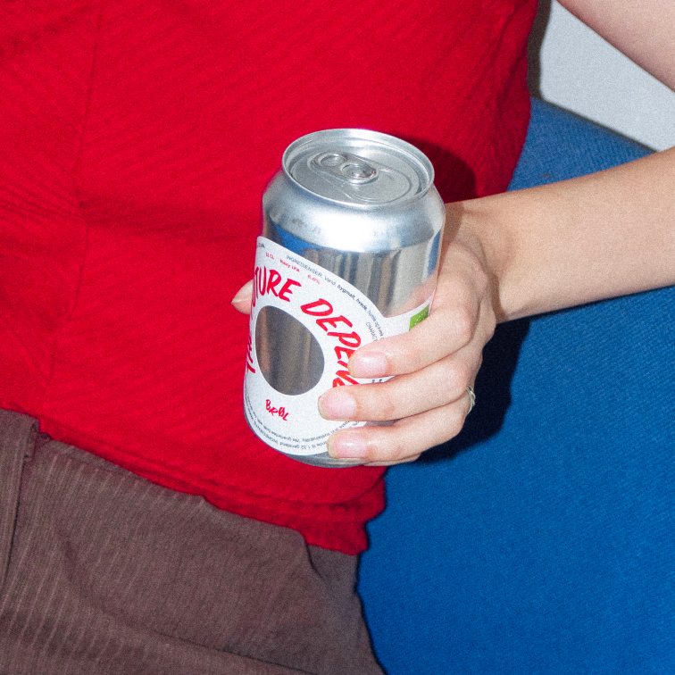 A BRØL can in hand, against a red shirt and blue seat